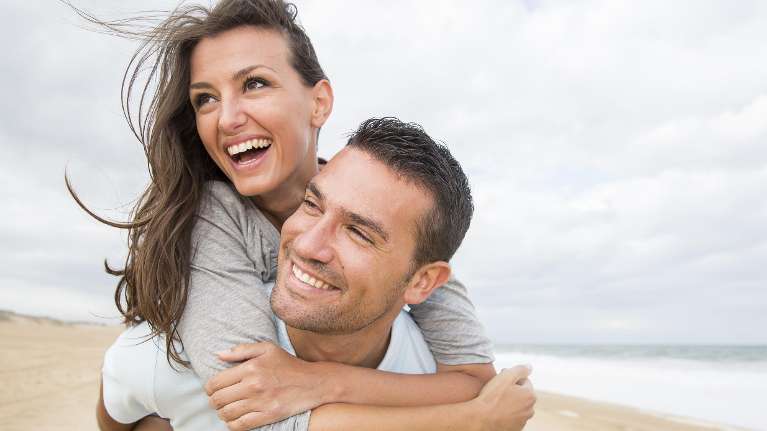 Happy couple smiling at the beach after cosmetic dental treatments in Hampton Park