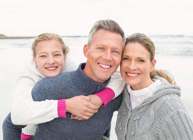 Smiling family with parents and daughter enjoying time outdoors, symbolizing healthy teeth and oral 