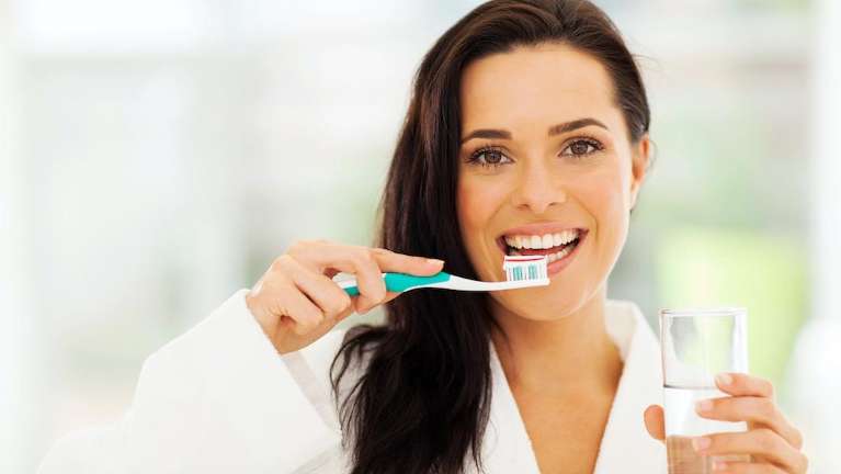 Woman brushing teeth at home to maintain dental implants and oral health in Hampton Park