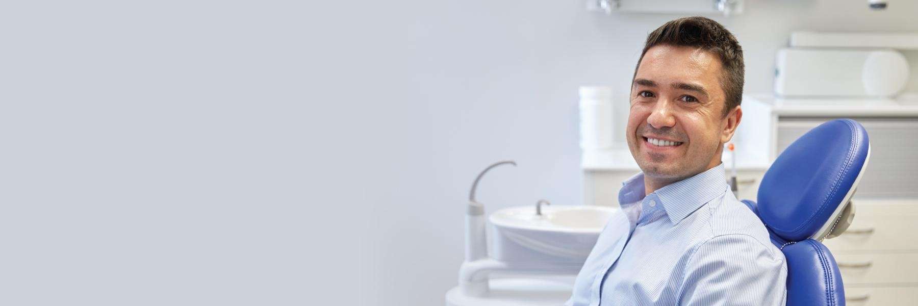Man smiling confidently while sitting in a dental chair during a check-up at a modern dental clinic.